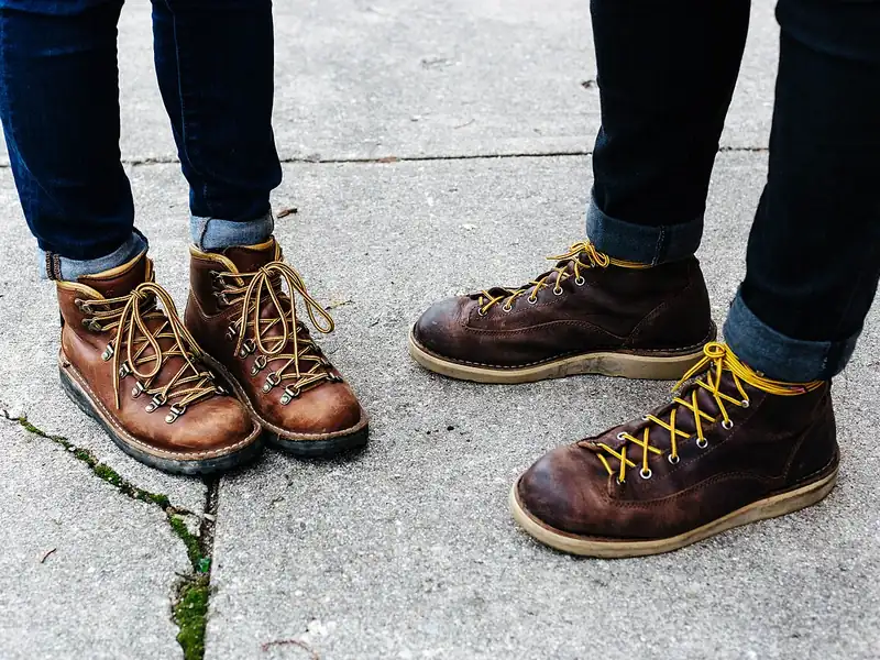Two people in laced leather boots on a sidewalk (illustrative photo)