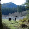 Two camp chairs by a river in a forest (illustrative photo)