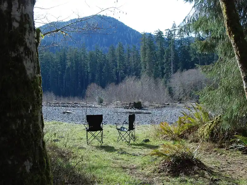 Two camp chairs by a river in a forest (illustrative photo)