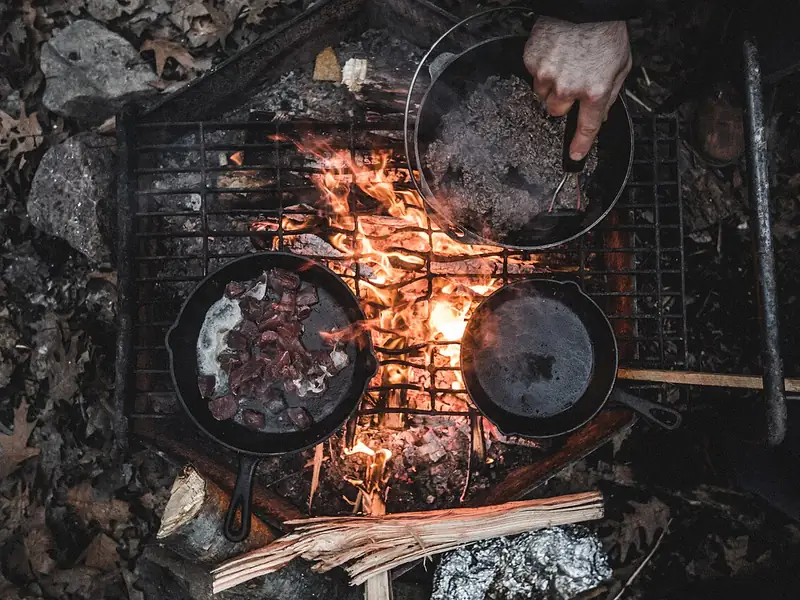 Cast-iron pans on a grill over a campfire (illustrative photo)