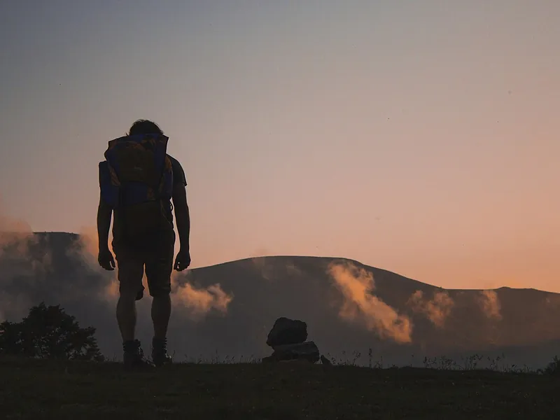Hiker with a backpack silhouetted on a hilltop at dusk (illustrative photo)