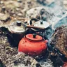 Camp kettles warming in campfire embers (illustrative photo)