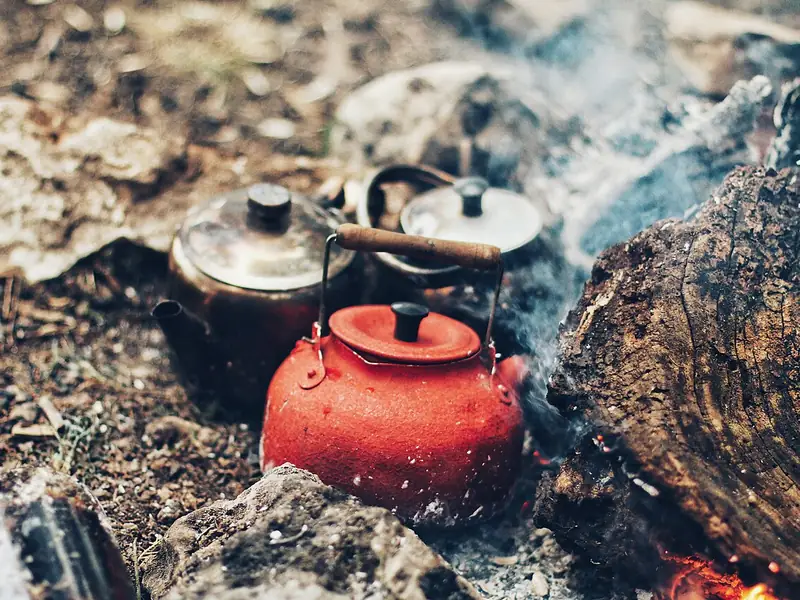 Camp kettles warming in campfire embers (illustrative photo)