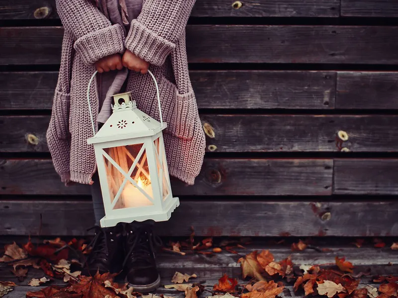 Person holding a white lantern with a candle (illustrative photo)