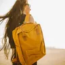 Person on a windy beach carrying a yellow backpack (illustrative photo)
