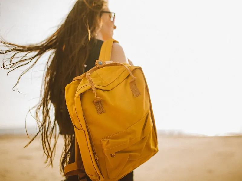 Person on a windy beach carrying a yellow backpack (illustrative photo)