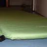 Green self-inflating sleeping pad on a floor (illustrative photo)