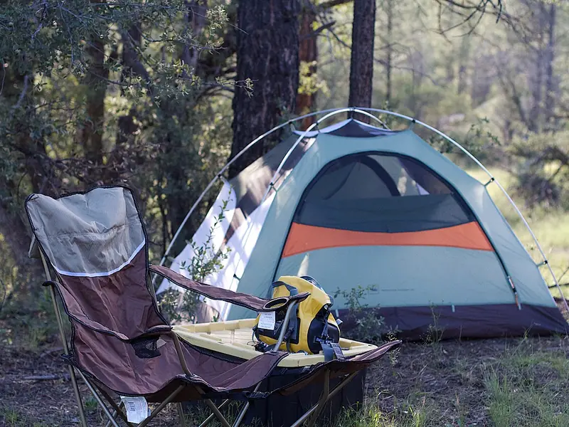 Dome tent with a camp chair at a forest campsite (illustrative photo)