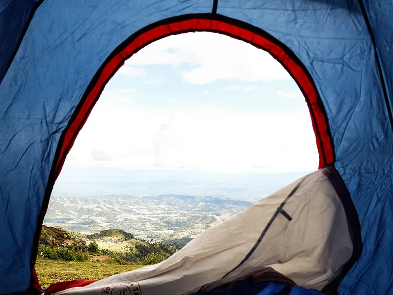 View out of a tent door past a sleeping bag to the hills (illustrative photo)