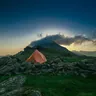 Orange tent on a rocky hillside at dusk (illustrative photo)