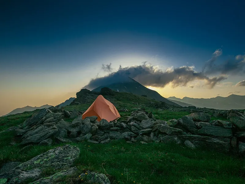 Orange tent on a rocky hillside at dusk (illustrative photo)