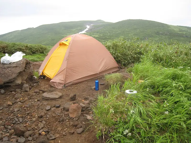 Orange dome tent on a grassy hillside (illustrative photo)