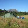 Green tunnel tent in a meadow below mountains (illustrative photo)