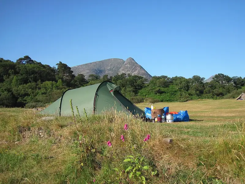 Green tunnel tent in a meadow below mountains (illustrative photo)