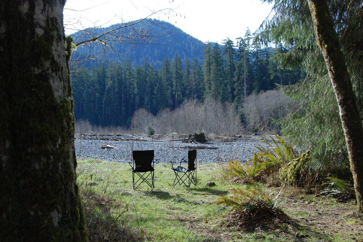 Two camp chairs facing a rocky riverbed in a forested valley