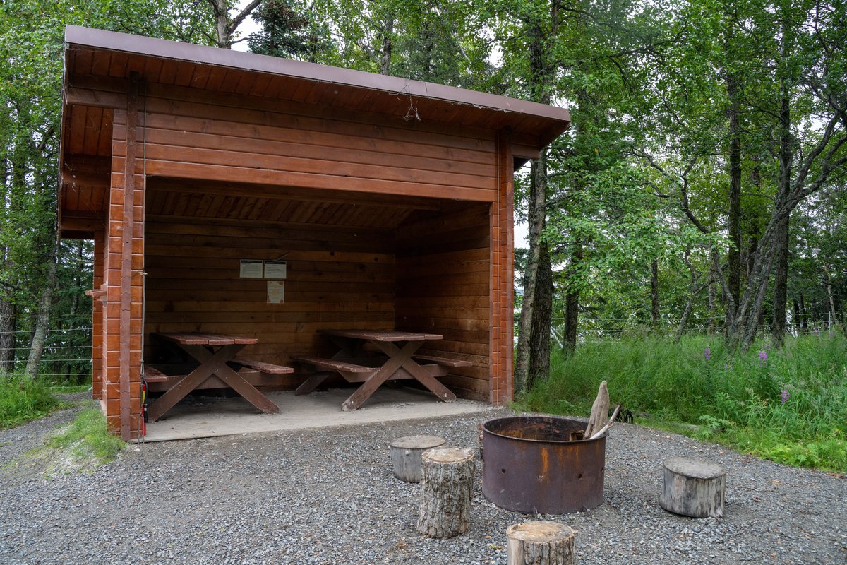 Wooden campground cooking shelter with picnic tables and a fire ring