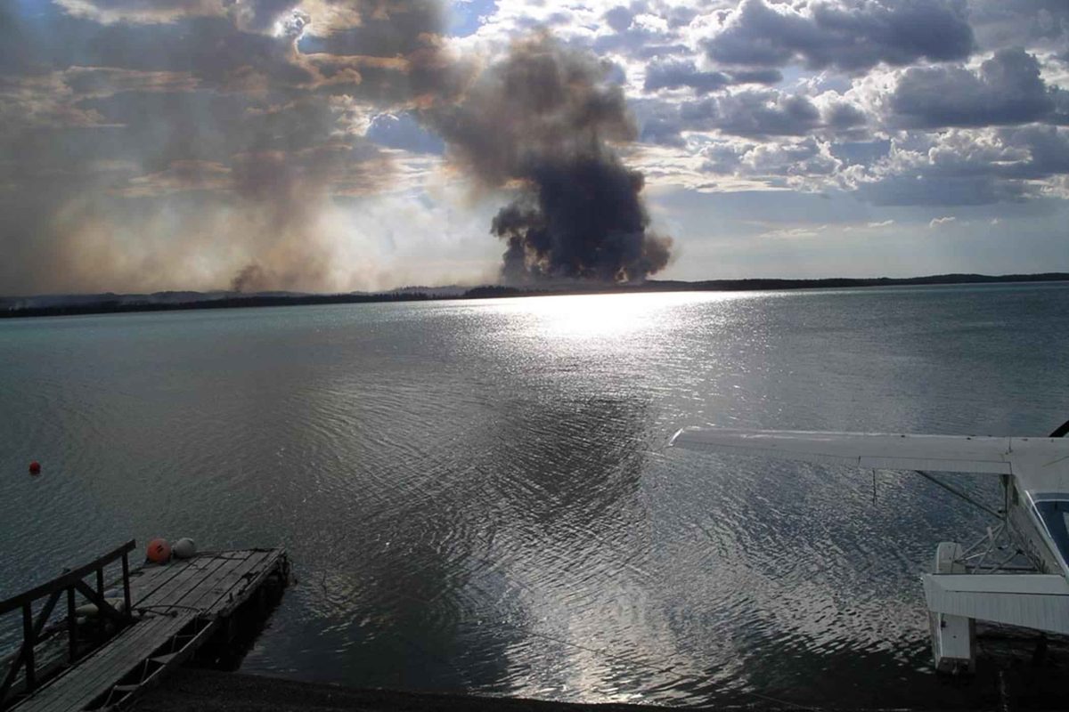 Illustrative photo of wildfire smoke rising beyond a lake, seen from a dock