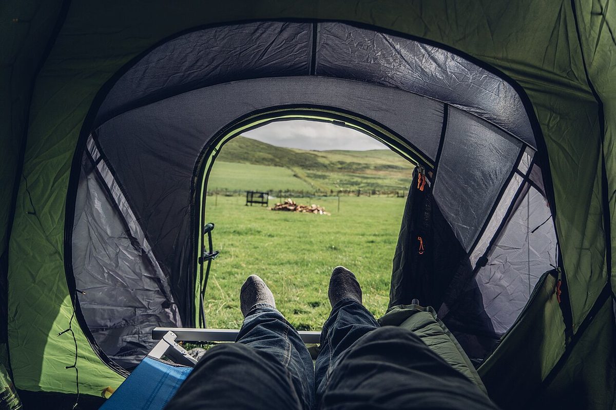 View from inside a green tent looking out the door toward a grassy field