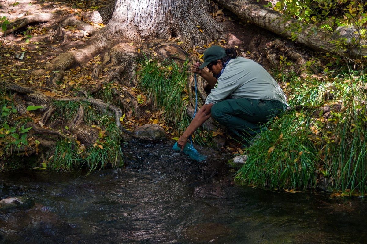 Illustrative photo of a hiker kneeling at a spring to refill a water reservoir