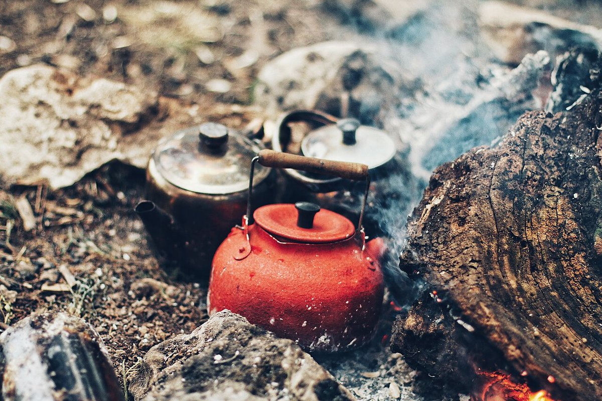 Camp kettles warming in campfire embers near a outdoor cooking setup