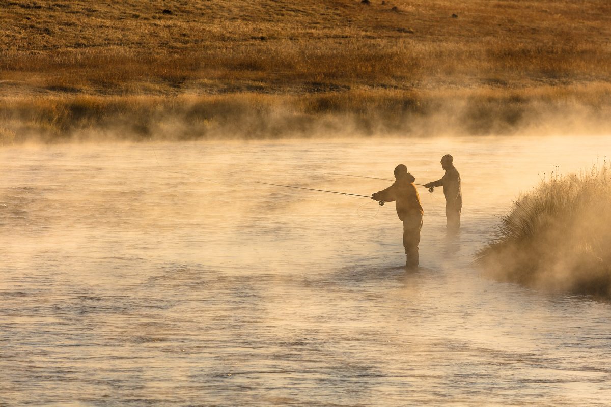 Illustrative photo of two anglers standing in a misty river at sunrise casting fly rods