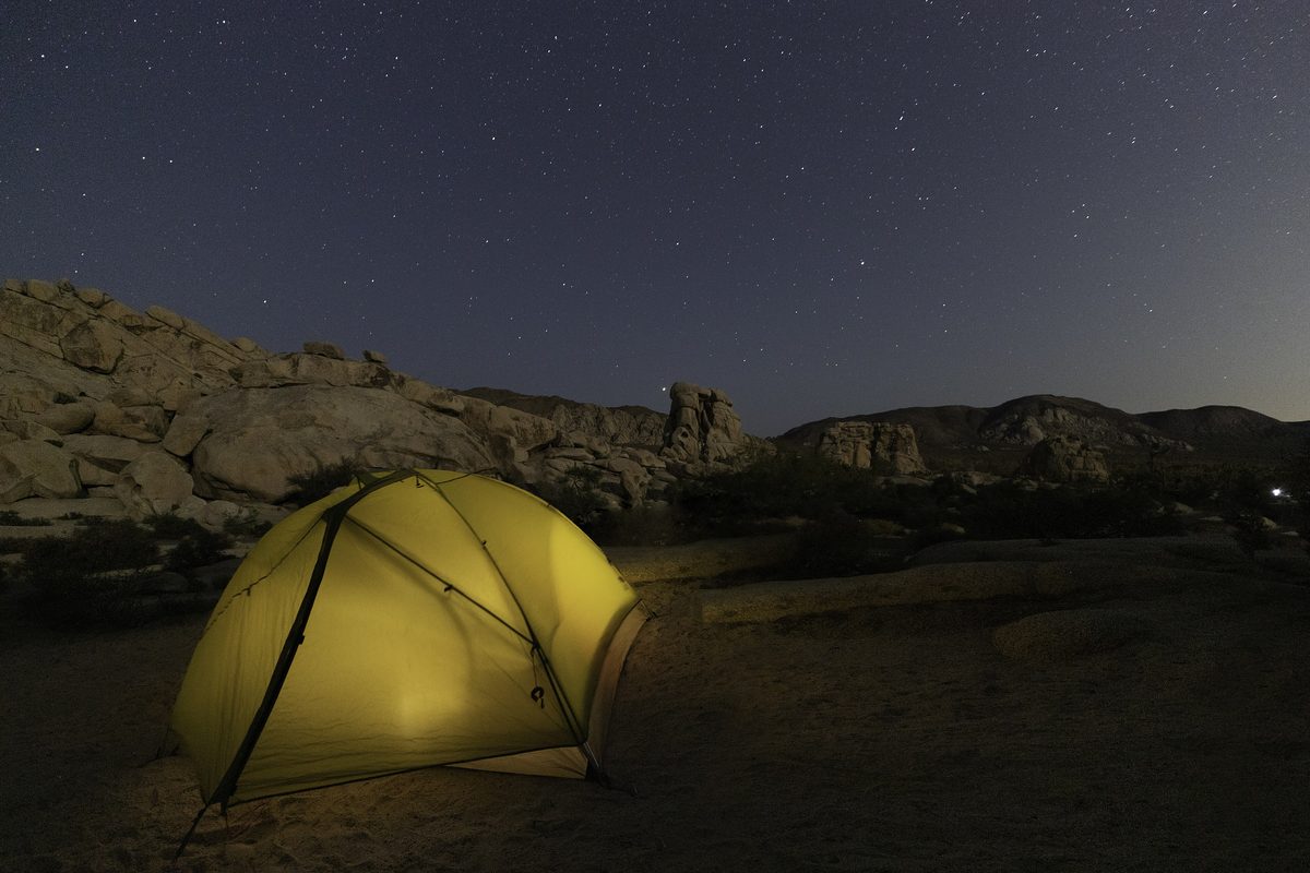 Illustrative photo of a yellow tent lit from inside beneath a starry sky at a desert campground