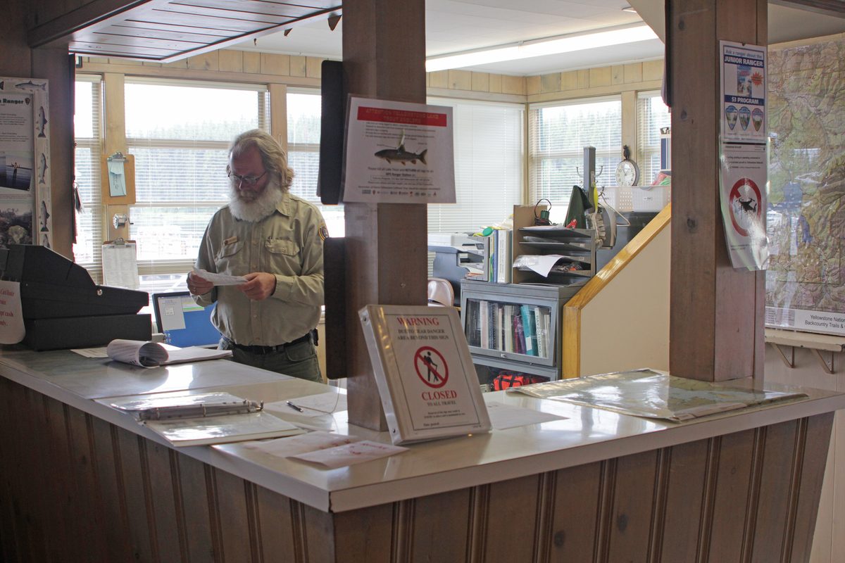 Illustrative photo of a park ranger standing behind the counter of a backcountry permit office with maps and information signs