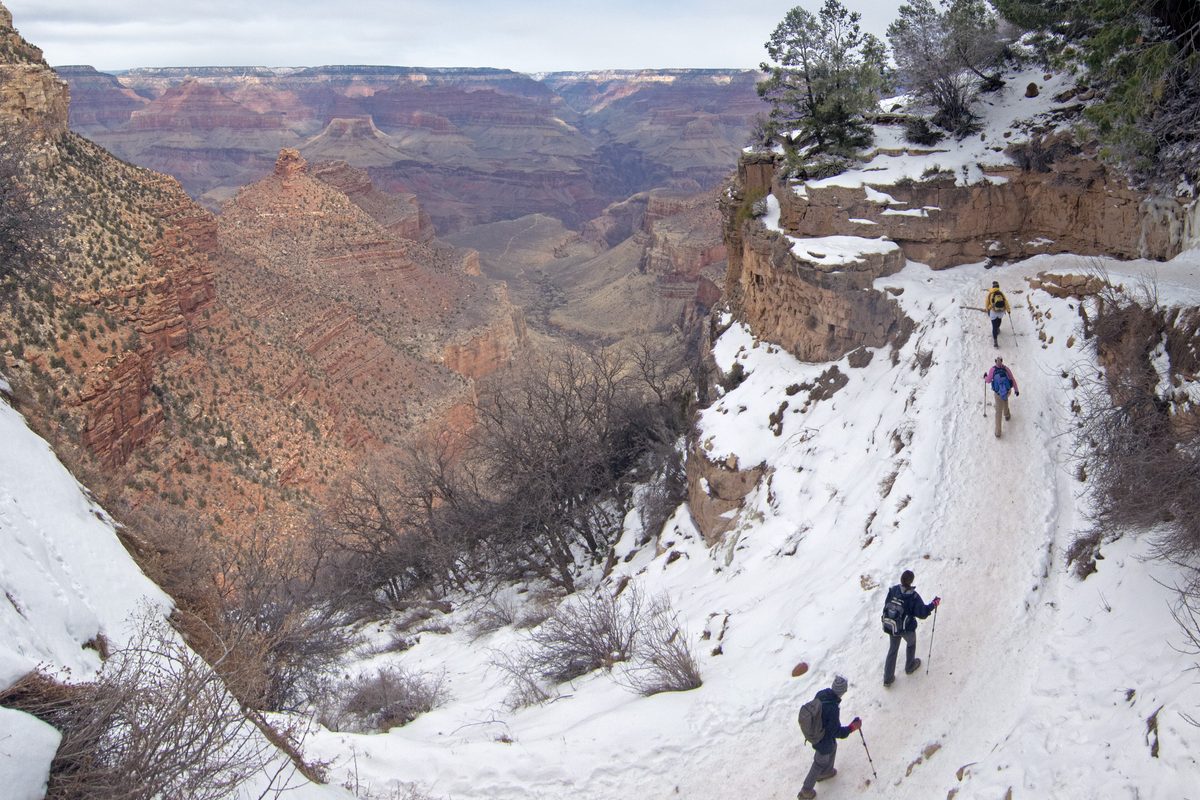 Illustrative photo of winter hikers walking down a snow-packed canyon trail lined with icy rock and pine trees