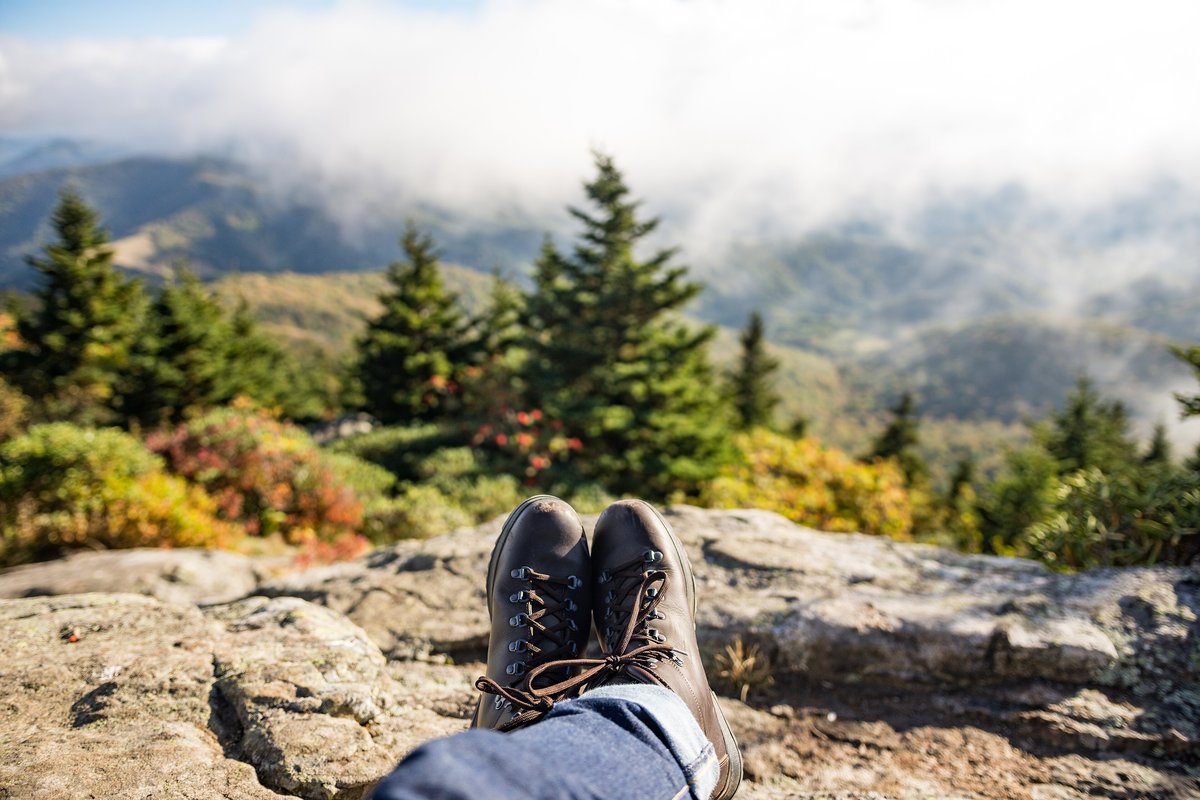 Hiker resting with boots crossed on a rock above a misty forested valley