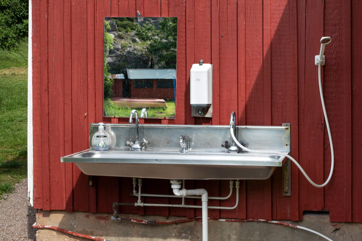 Illustrative photo of an outdoor wash sink with a soap dispenser and mirror on a red campground utility building