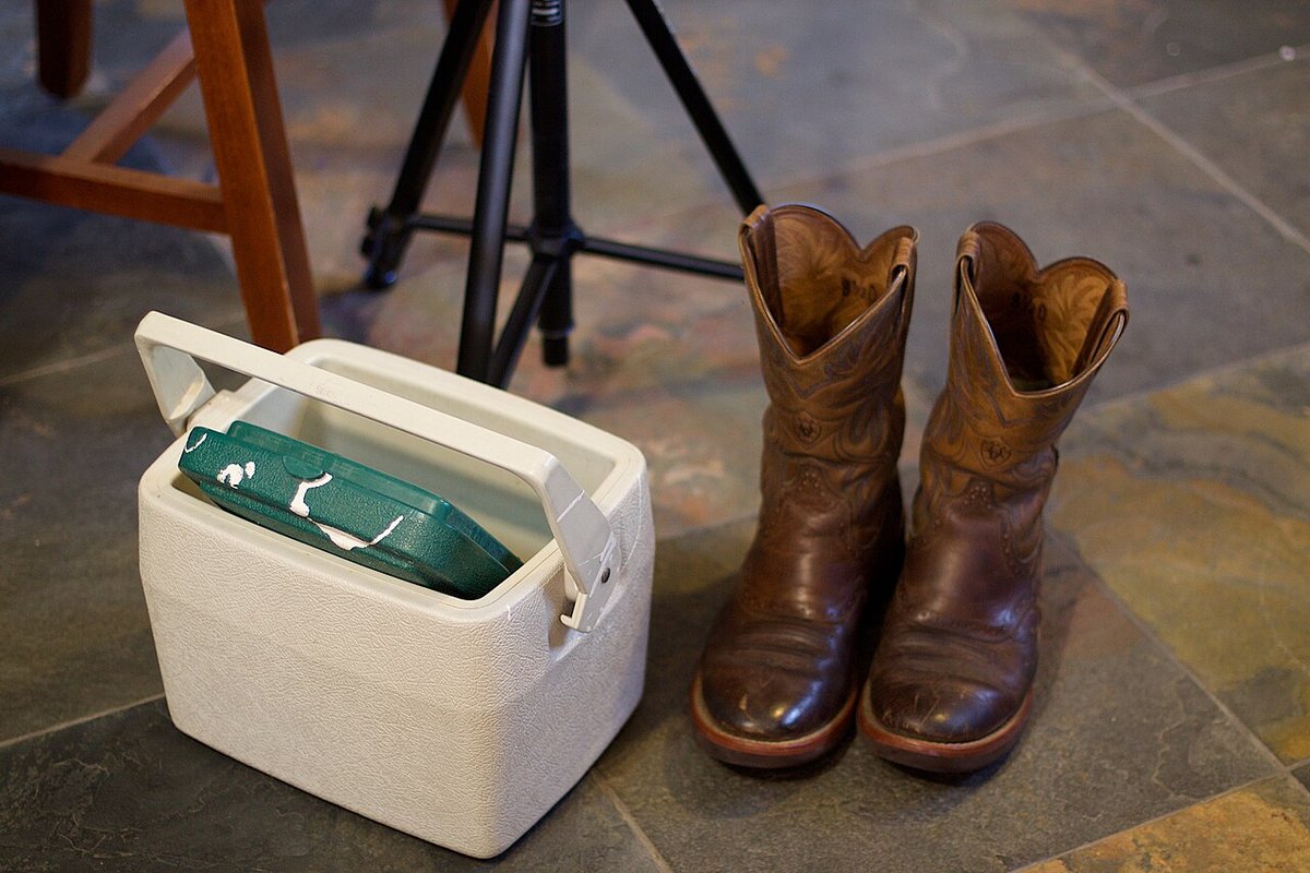 Open cooler packed with ice and camping food on grass beside boots