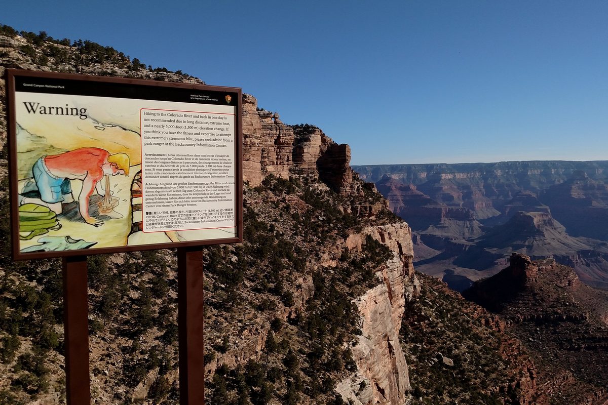Illustrative photo of a heat illness warning sign beside a canyon trail on a hot, cloudless day