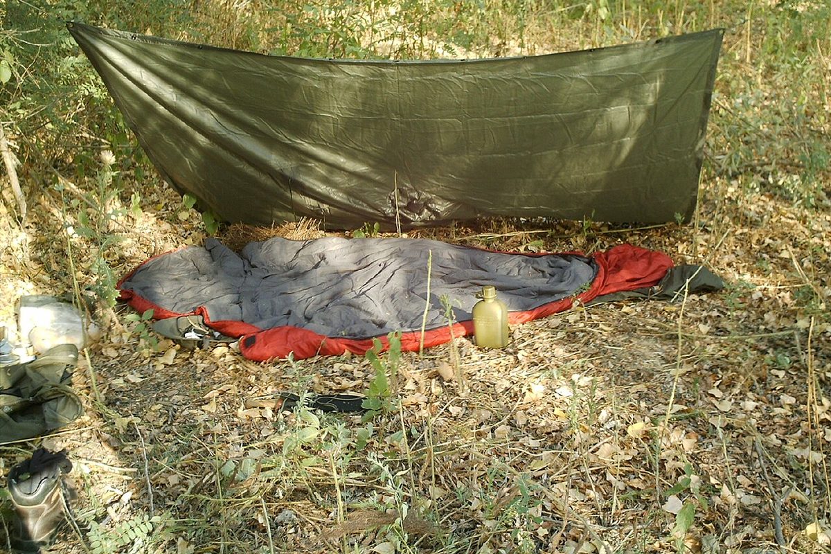 Green tarp pitched low over a sleeping bag on dry grass
