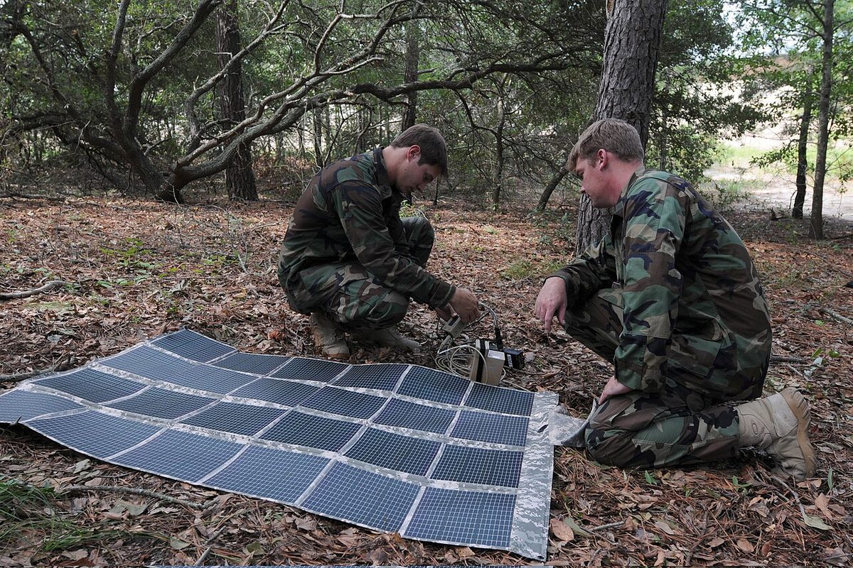 Two people setting up a folding solar panel mat on the forest floor