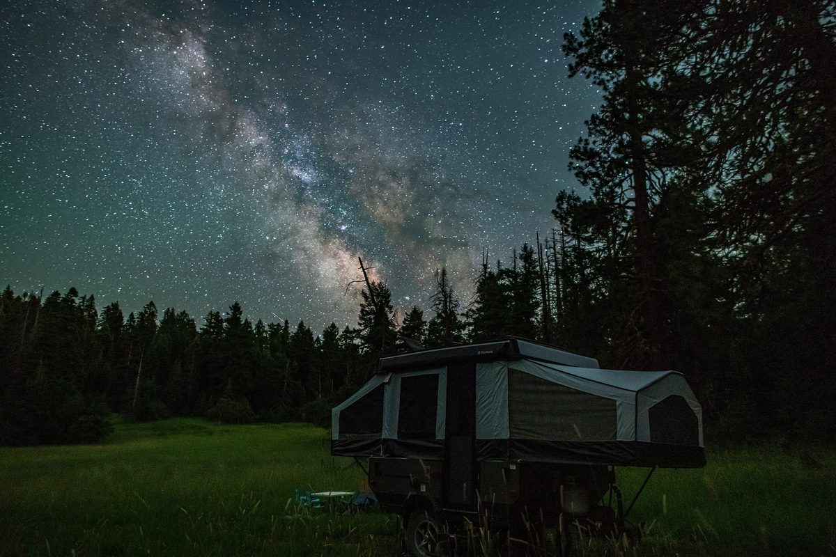 Illustrative photo of the Milky Way over a pop-up camper at a forest campsite