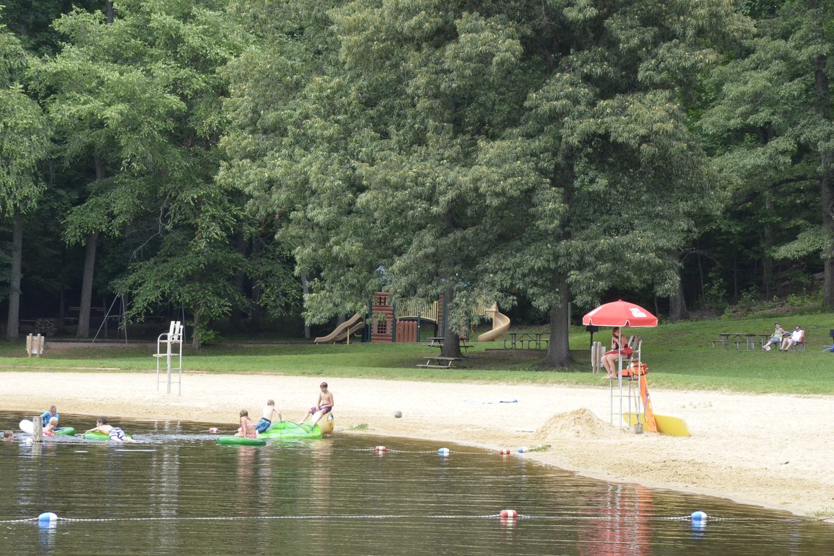 Illustrative photo of a roped-off swimming beach on a wooded lake with a lifeguard stand and children playing in the shallows