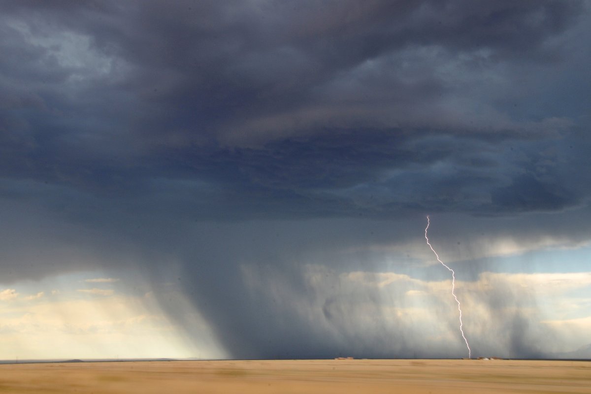 Dark thunderstorm with a lightning bolt and rain over open farmland